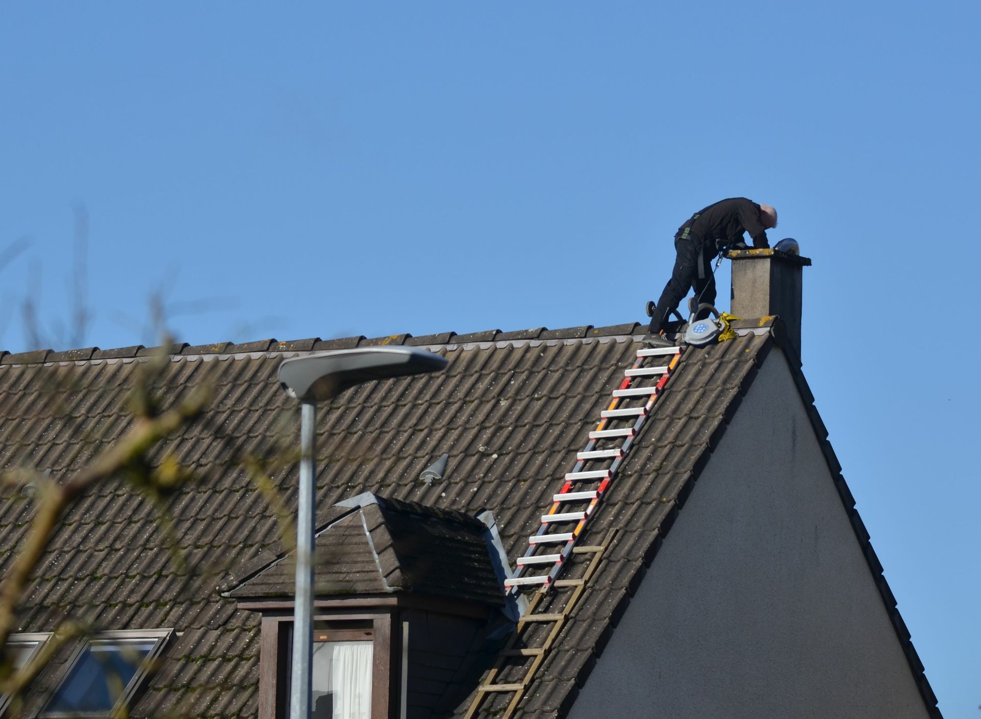 Man on roof near chimney with ladder.