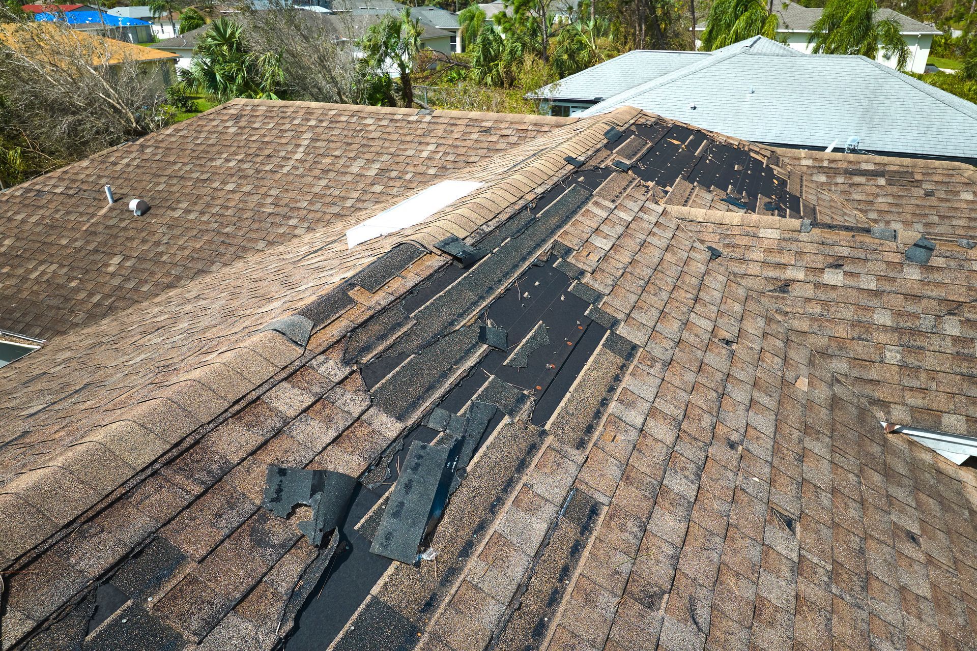 Damaged asphalt shingle roof, with missing and torn shingles, showing the underlayment.