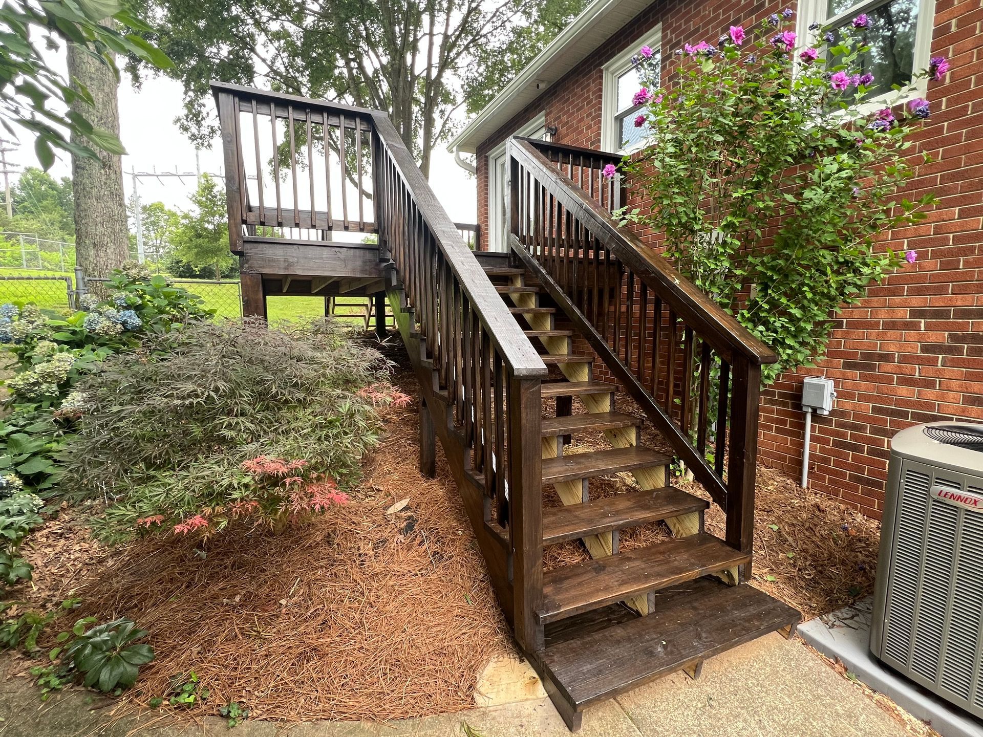 Wooden deck with stairs leading up to it, adjacent to a brick house.