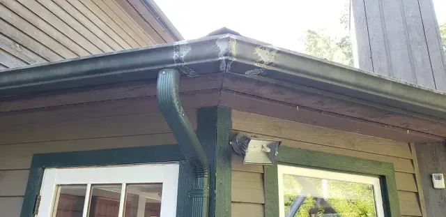 Corner of a house with green gutters and downspout, next to a window and a security light.