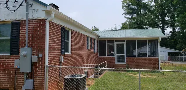 Brick house with screened porch, metal roof, and chain link fence on a cloudy day.