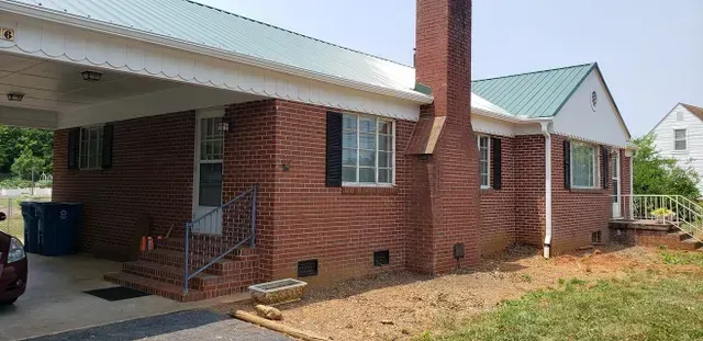 Red brick house with a green metal roof and a carport.