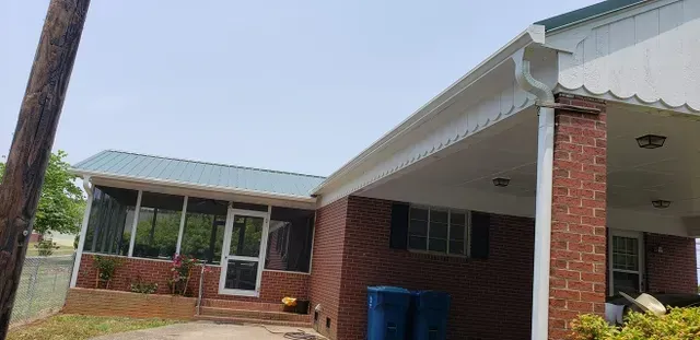 A brick house with a green metal roof and a screened-in porch. The sky is visible.
