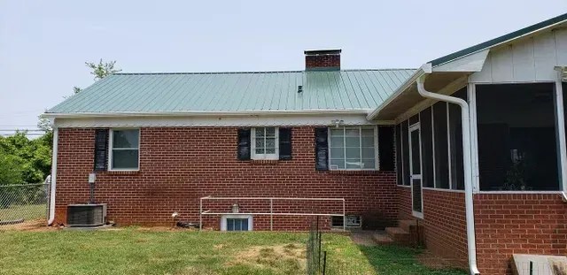 A brick house with a green metal roof, a screened-in porch, and a chimney.