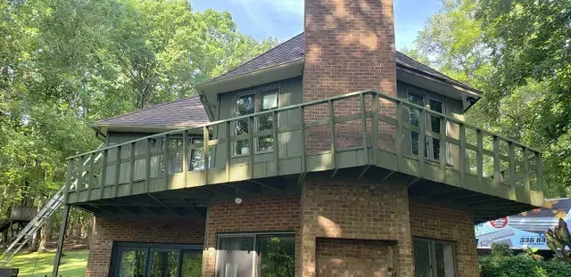 House with brick exterior and green balcony surrounded by trees.