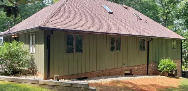 A house with a brown roof and green siding. The house is on a slight hill and has a small garden bed in front.