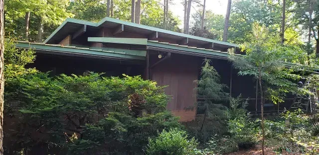 A brown house with a green roof surrounded by trees and lush greenery.