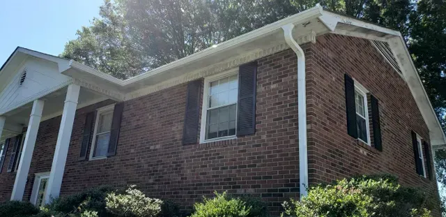 Brick house with white trim, black shutters, and green bushes.