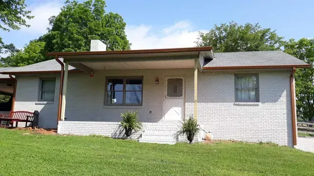 A one-story house with a white brick exterior, brown trim, and a porch. Green lawn in front.