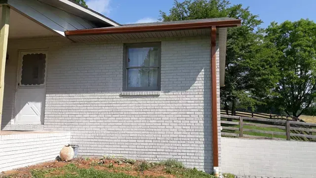 Light gray brick house exterior with brown gutters and trim, window, and white door.