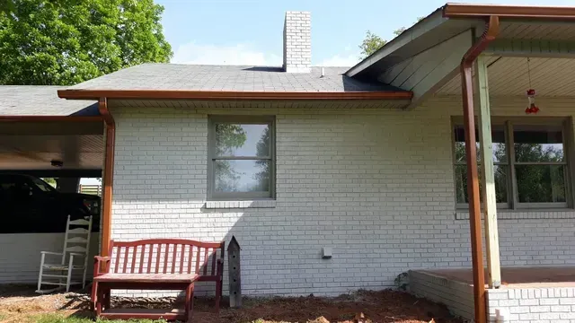 White brick house with brown gutters and a red bench outside.