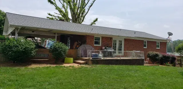 Red brick house with a covered patio, deck, and green lawn.