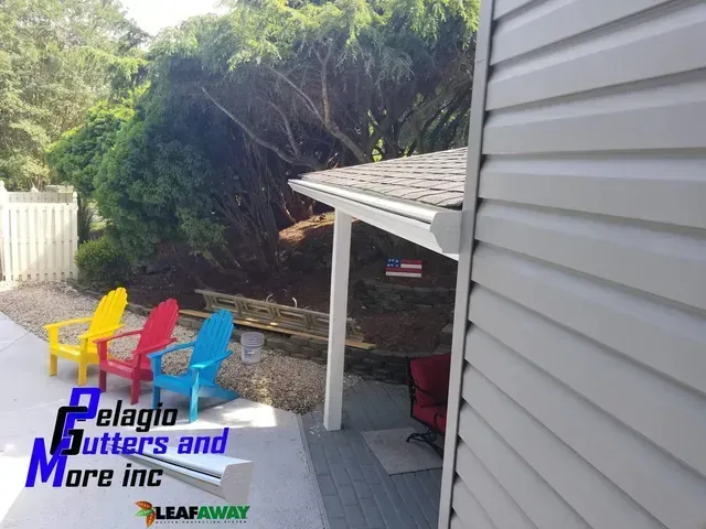 House with new white siding and gutters. Colorful chairs sit on a patio.