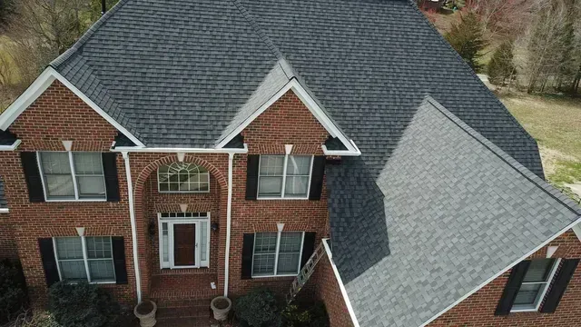 Brick house with dark gray shingle roof. White trim, black shutters, and brown front door.