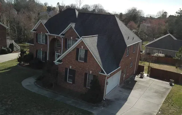Brick house with dark roof and attached garage, surrounded by grass and trees, on a sunny day.
