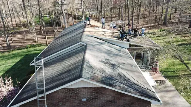 People working on a roof, preparing for repairs. Brick home, surrounded by trees.
