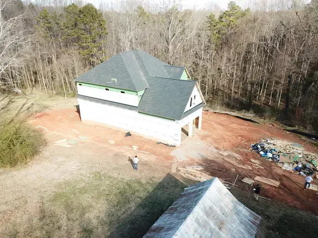 House under construction with framing and roof completed, surrounded by trees.