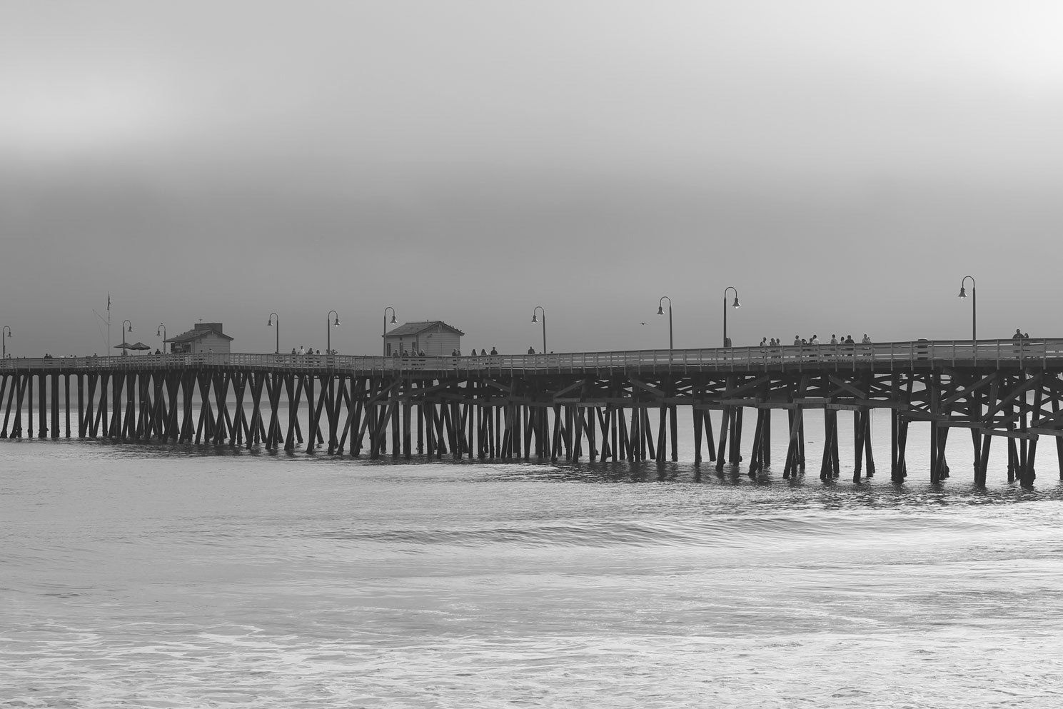 A pier extending over ocean water, people walking, overcast sky.