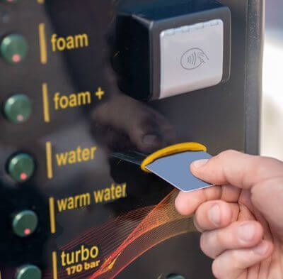 hand is holding a card in front of a carwash paystation