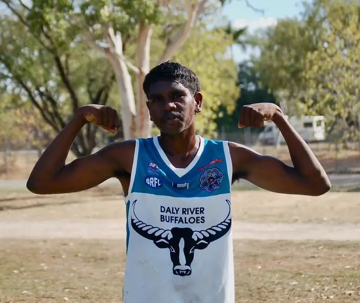 A man in a Daly River Buffaloes jersey flexes his biceps in a park.