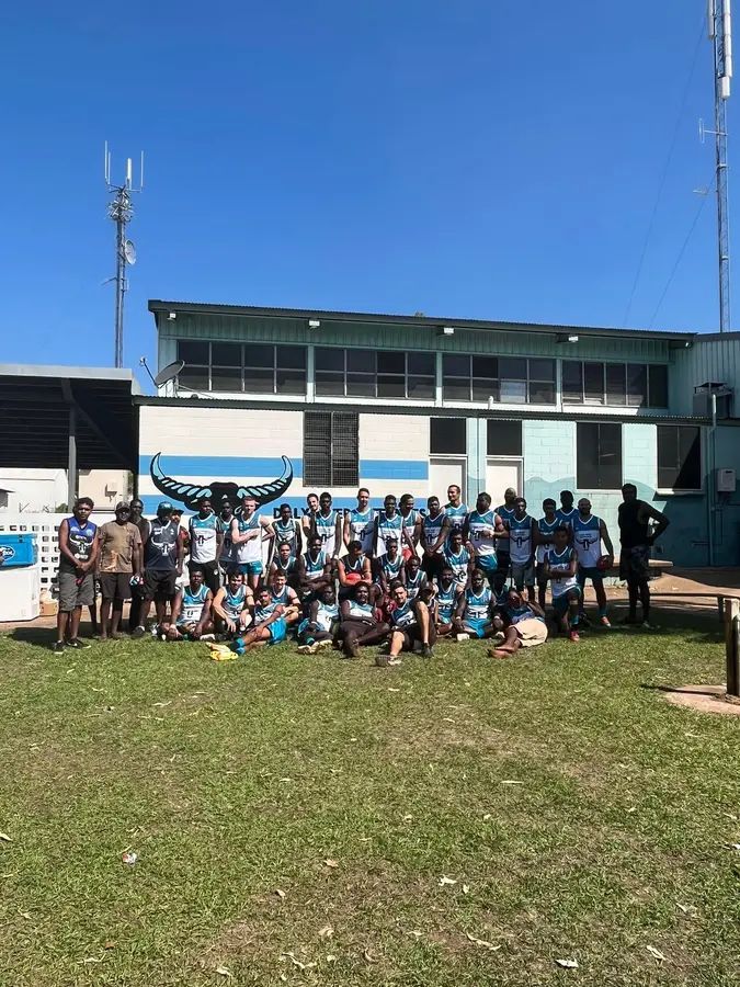 Group of people in blue jerseys pose outside a building on a sunny day.