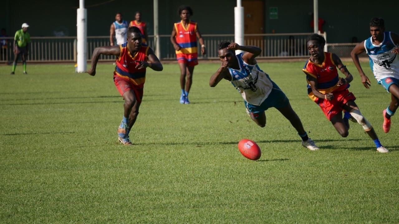 Football players in action on a green field. One dives for the red ball. Others run and wear colorful jerseys.