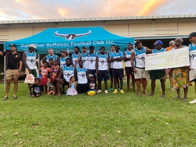 Football team, Dale River Buffaloes, holding a large check, celebrating outside under a tent; several spectators are present.