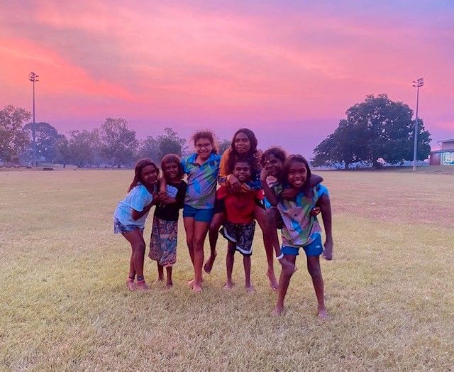 A group of Indigenous children smiling and posing on a grassy field at sunset.