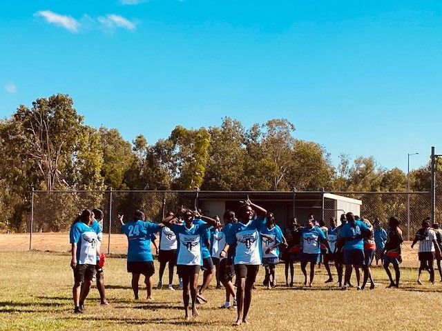 Group of people in blue and white shirts cheering on a grassy field under a blue sky.