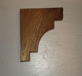 Wooden shelf bracket mounted on a light gray wall, brown wood grain visible, simple design.