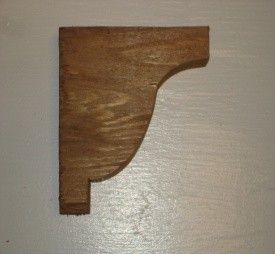 Wooden bracket with a curved edge and a square top and bottom, against a white surface.