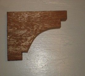 Brown wooden shelf bracket mounted on a light-colored wall, with a curved decorative design.