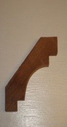 Wooden stair bracket against a white wall, brown color, curved design.