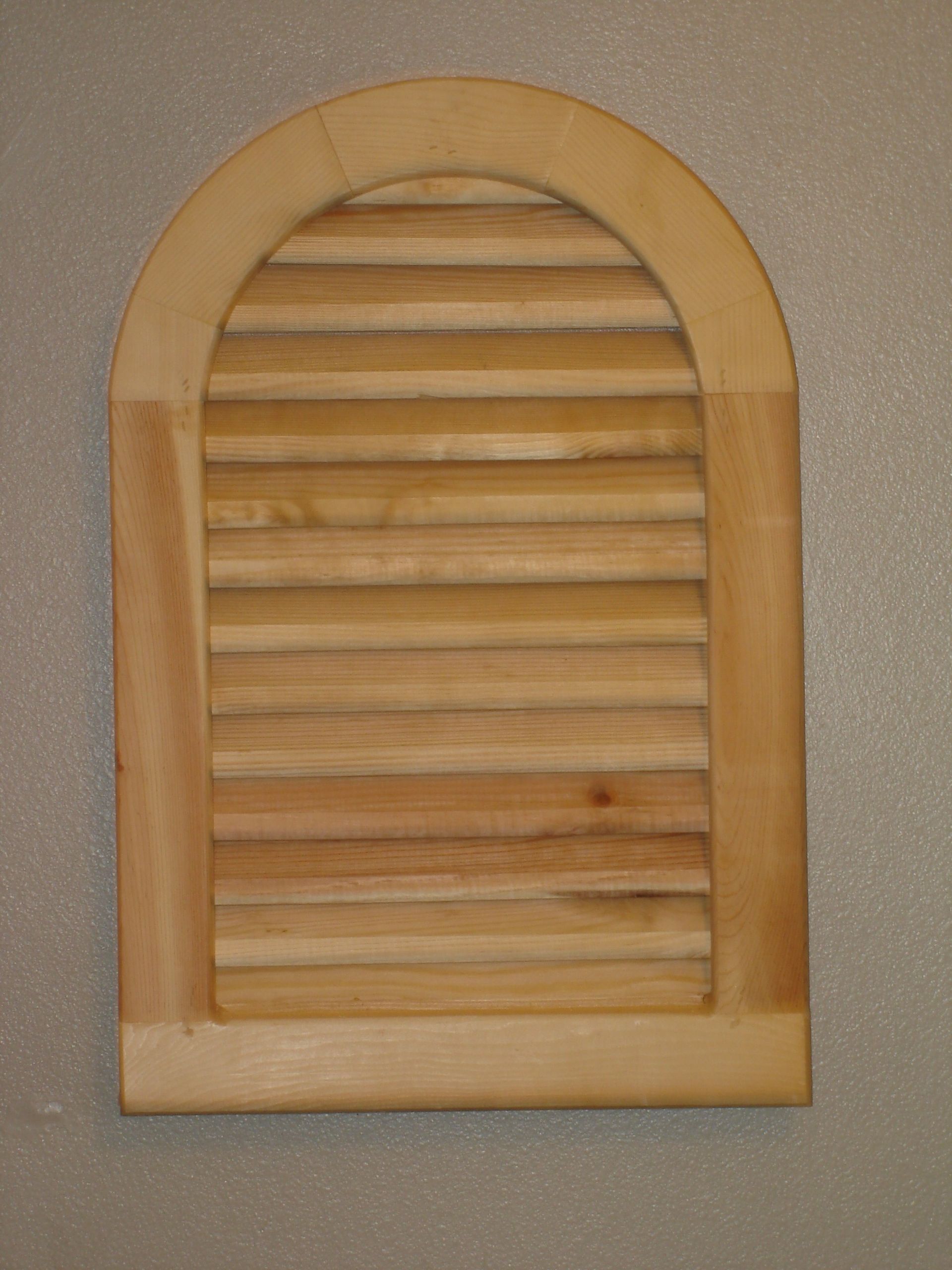 Wooden arched window shutter with horizontal slats on a gray wall.