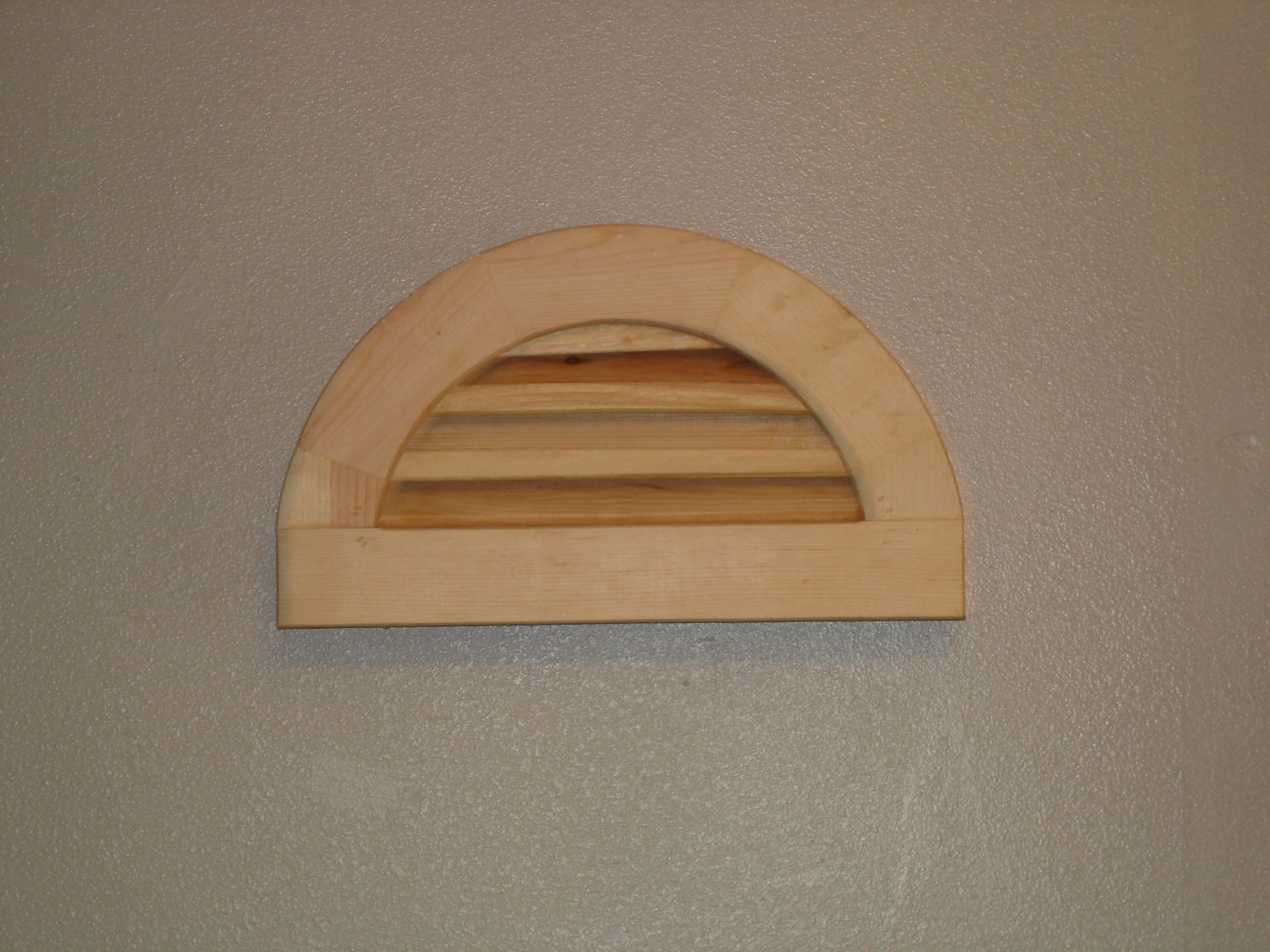 Wooden half-circle vent on a textured gray wall. It has horizontal slats for ventilation.