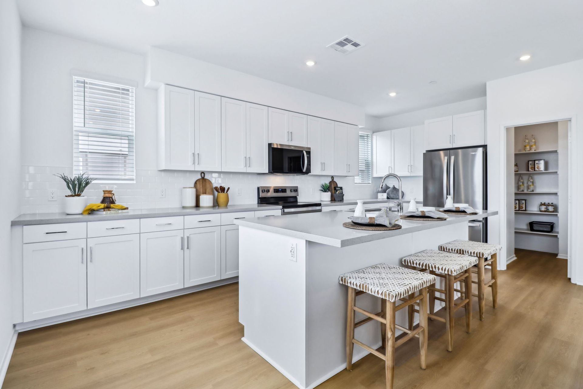 Bright, modern kitchen with white cabinets, island with stools, stainless steel appliances, and light wood flooring.