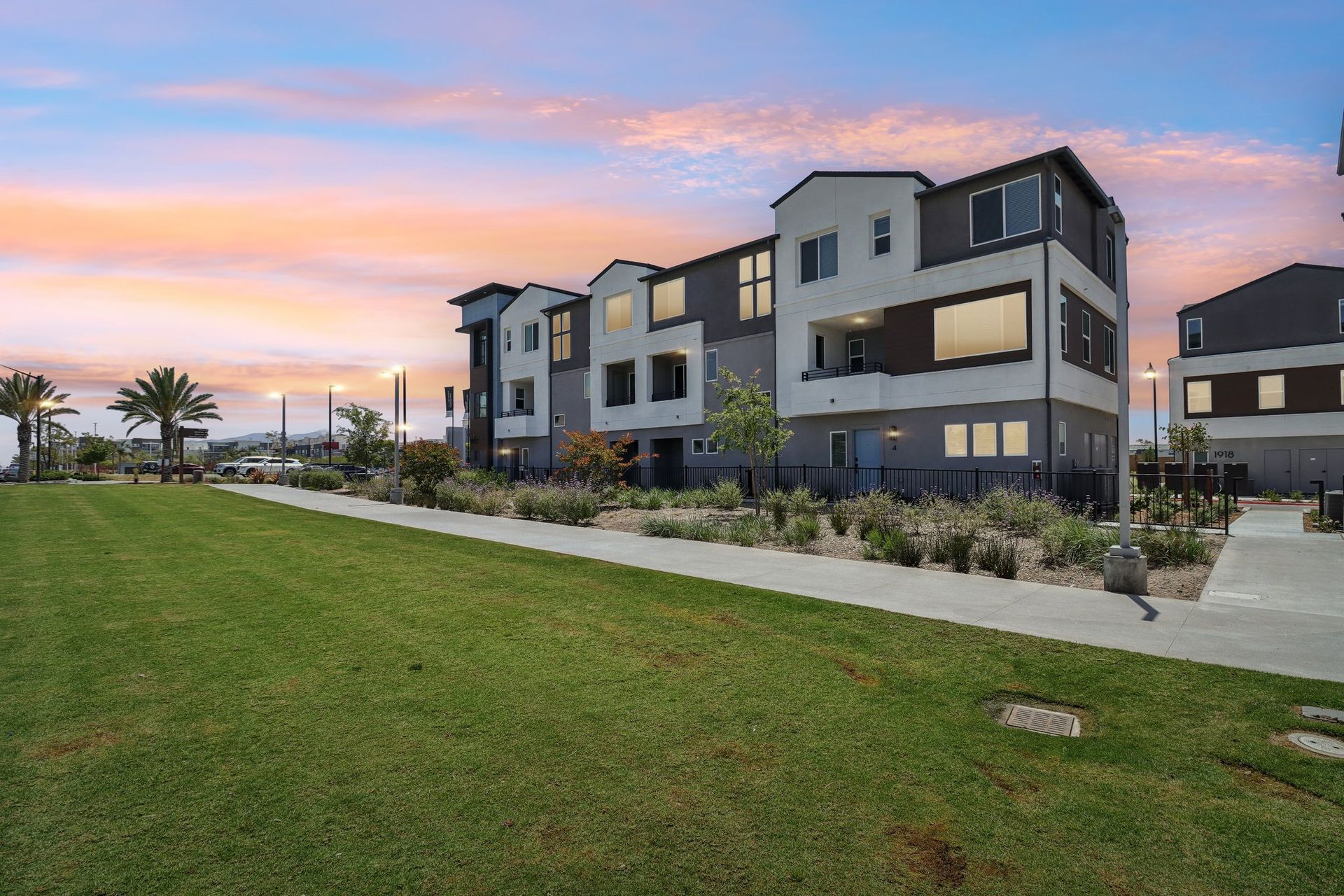 Modern townhouses with green lawn, walkway, and colorful sunset.