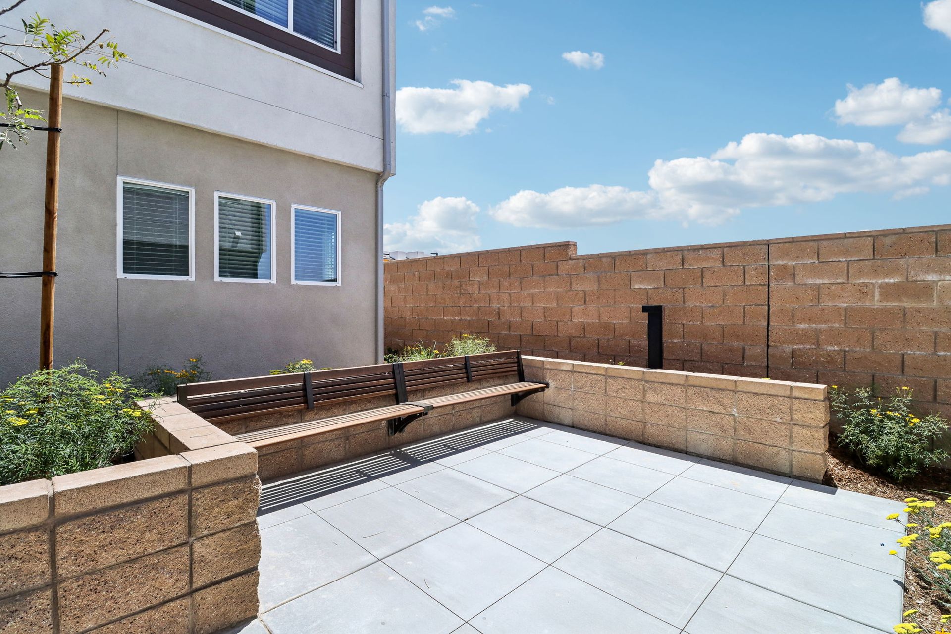 A patio with a bench and a brick wall in front of a house.