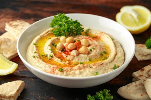 A bowl of hummus with chickpeas and parsley on a wooden table.