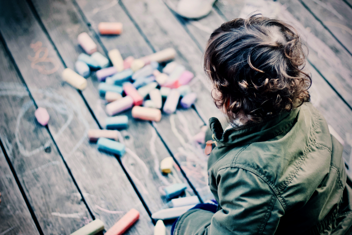 Child drawing with colorful chalk on a wooden surface.