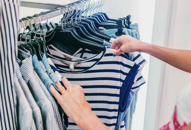 Person browsing a rack of clothing, focusing on a striped blue and white top.
