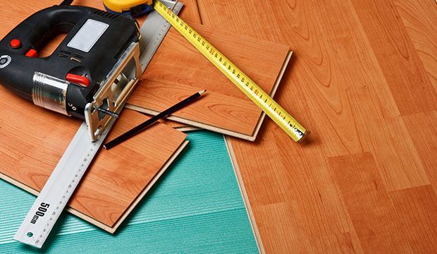 Una regla, una cinta métrica y una sierra están sobre un piso de madera.