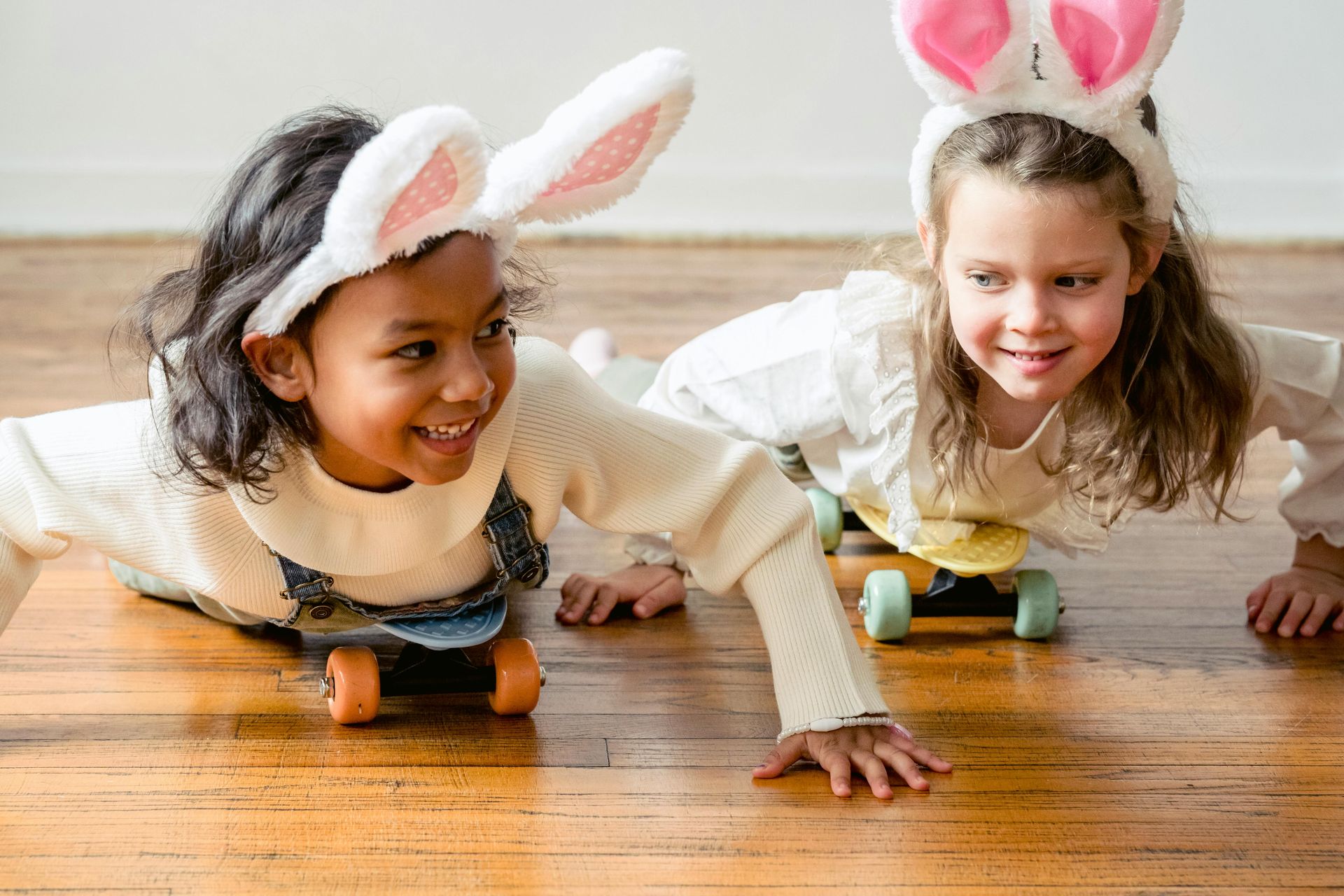 Two little girls in bunny costumes are playing on a wooden floor.