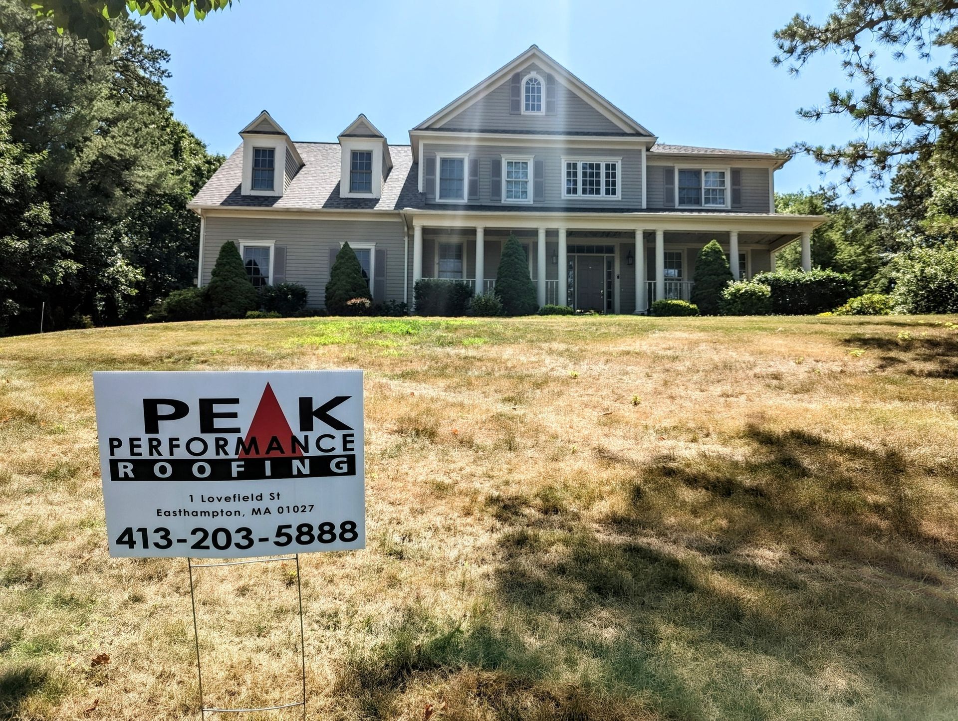 A large house with a peak performance roofing sign in front of it