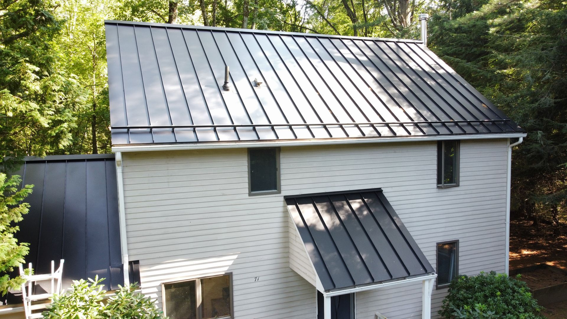A white brick house with a black metal roof surrounded by trees.