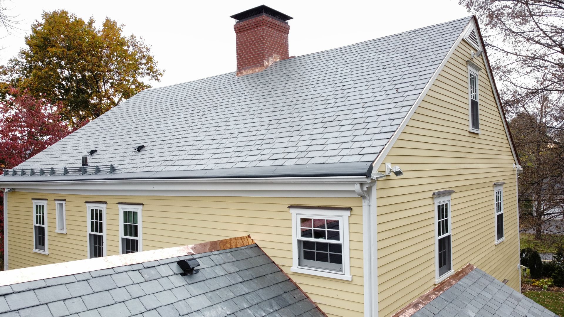 A yellow house with a gray roof and a chimney