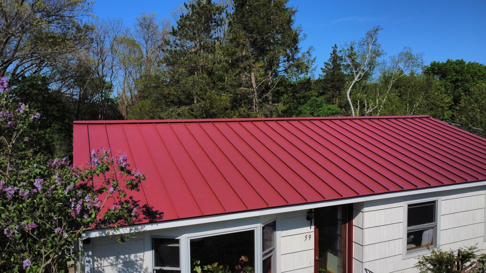 A white house with a red roof is surrounded by trees.