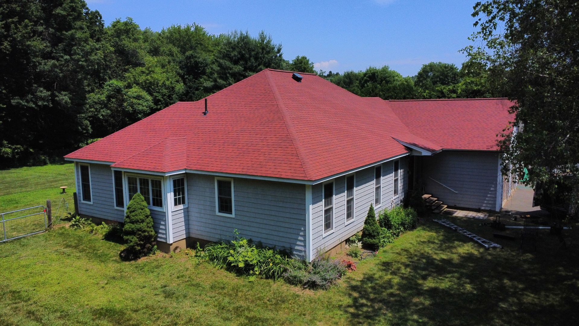 A white house with a red roof is surrounded by grass and trees.