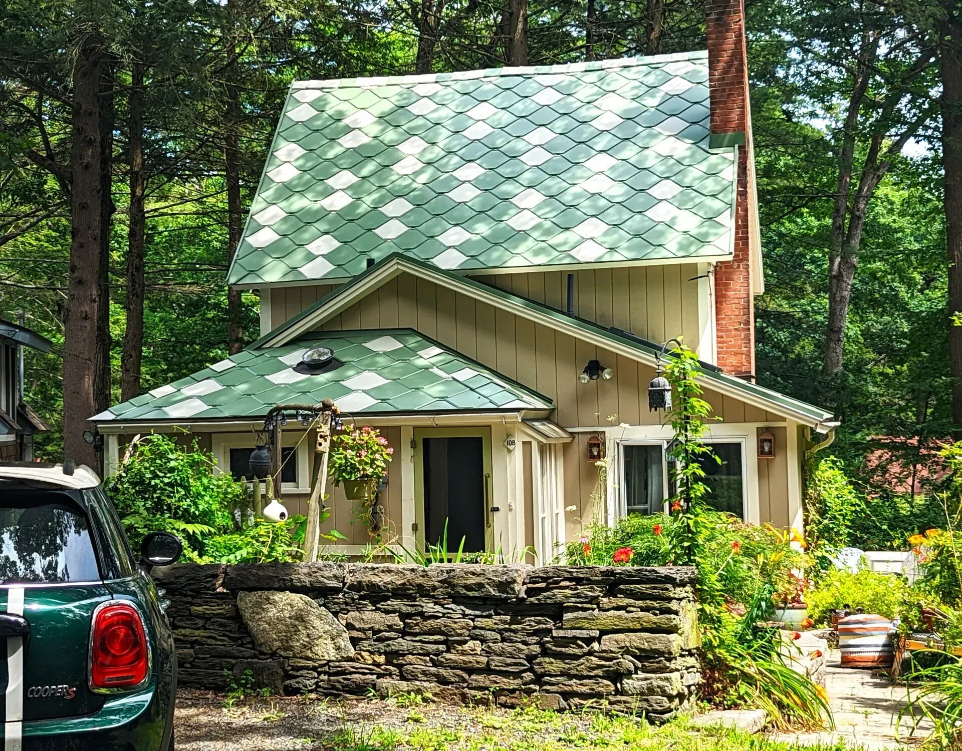 A green car is parked in front of a house with a green roof