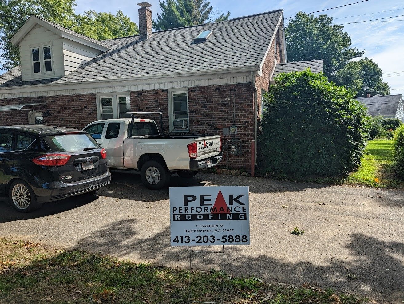 A white truck is parked in front of a brick house.